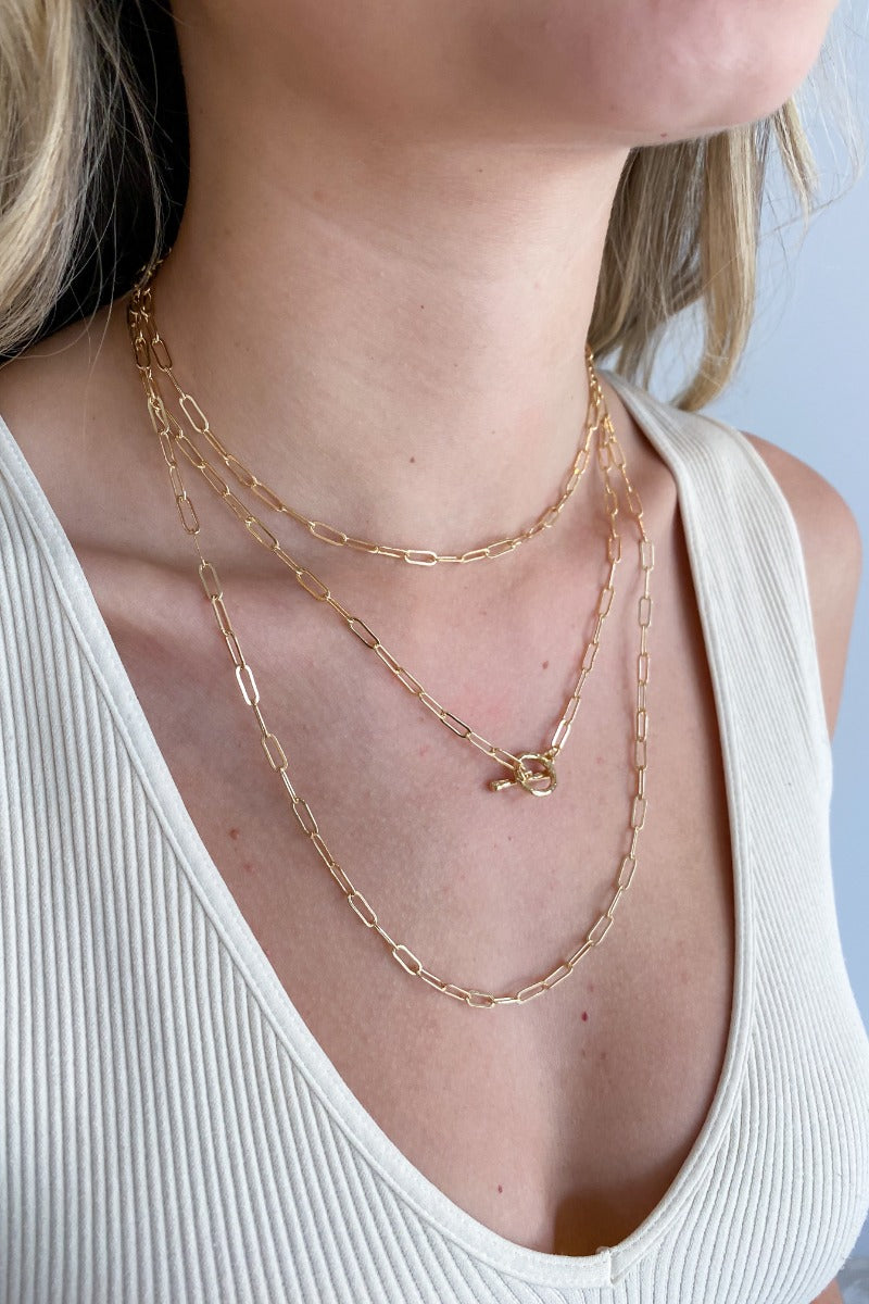 Close up view of model wearing the One Last Time Necklace which features triple layer with gold chain links and an open circle. 