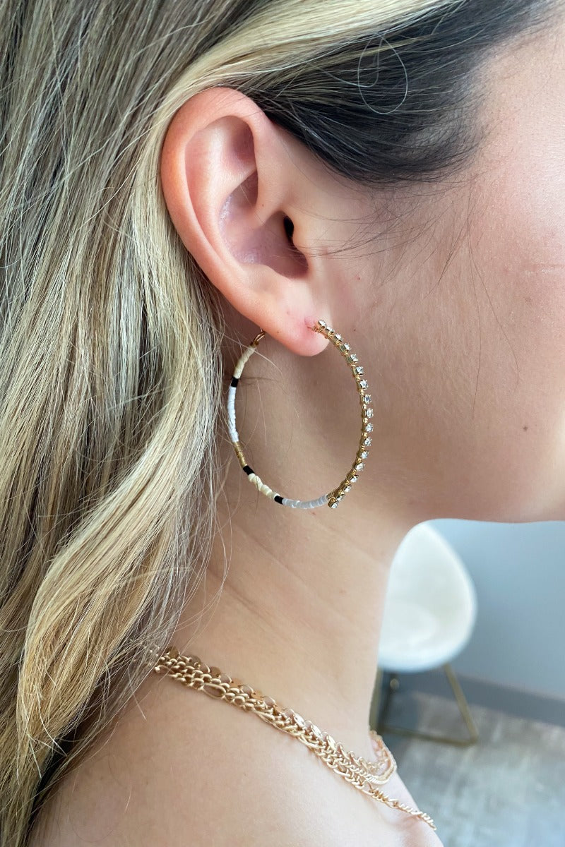 Side view of model wearing the Never Let Me Down Earrings which features gold hoops with black, gold, natural and white beads with clear stones.