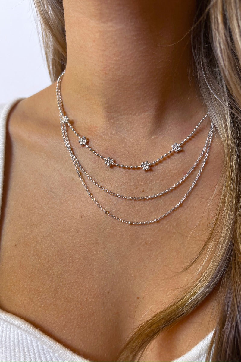 Front view of model wearing the Send Flowers Necklace in Silver which features triple-layered silver chain link with silver beaded flowers.