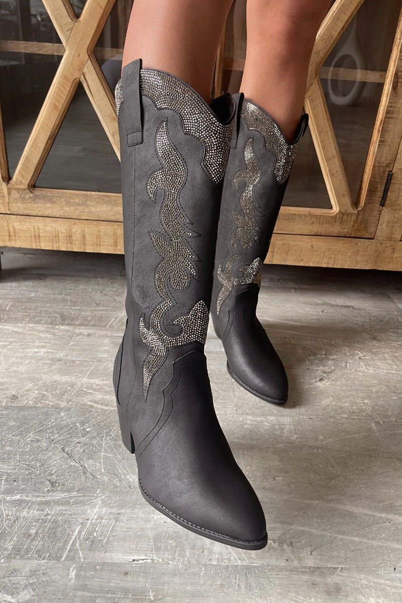 Front view of model wearing the Zane Rhinestone Cowgirl Boot in Black which features a western style pattern with rhinestone details, tall boot, pull tabs, monochromatic heel and chic pointed toe.
