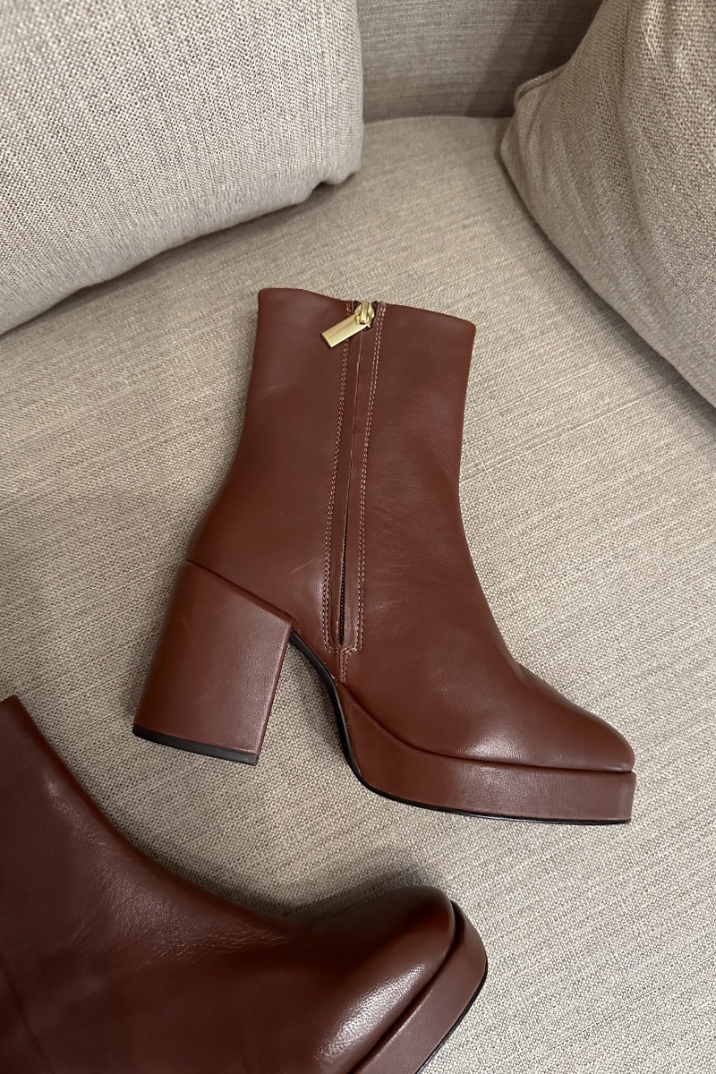 Close up front lay view of the Sweet Lady Leather Boot in Brown which features brown leather upper fabric, monochrome rubber sole, block heel, square toe and inside side zipper closure. 