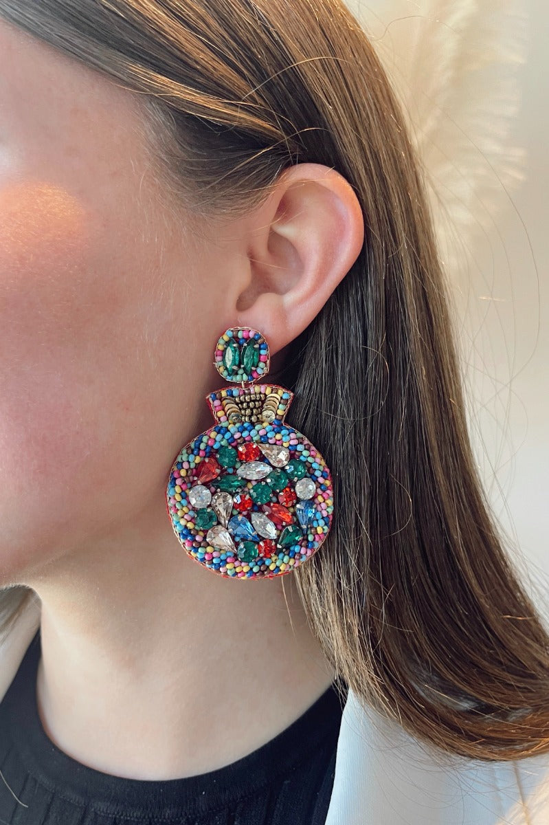 Close up view of model wearing the Put A Ring On It Earrings which features multi color stones embellished ring shaped.