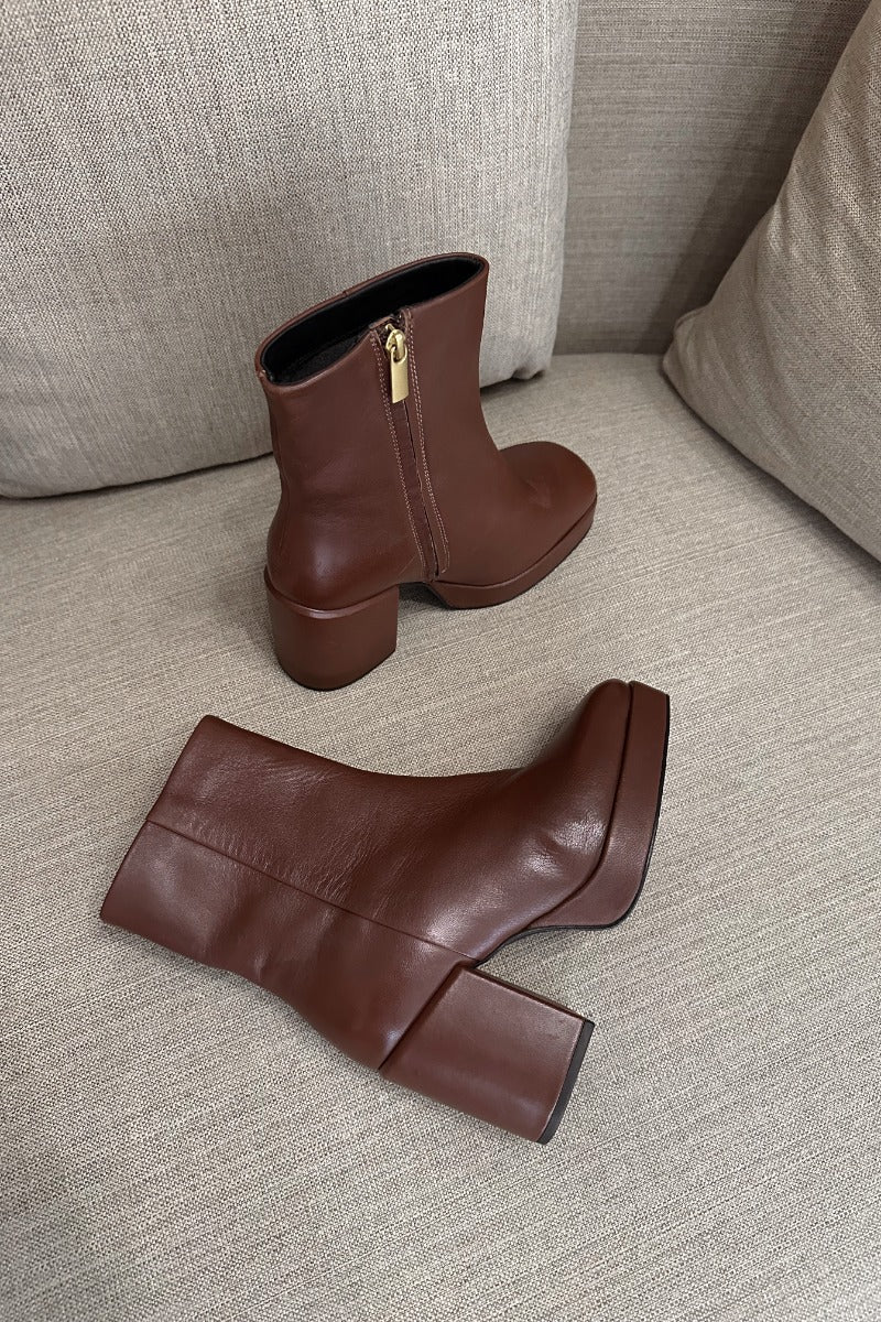 Front lay view of the Sweet Lady Leather Boot in Brown which features brown leather upper fabric, monochrome rubber sole, block heel, square toe and inside side zipper closure. 