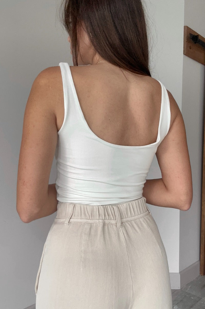 Back view of model wearing the Josie Off White Basic Scoop Neck Tank that has stretchy double-layered off white knit fabric, an elastic hem, a scooped neckline, and thick straps.