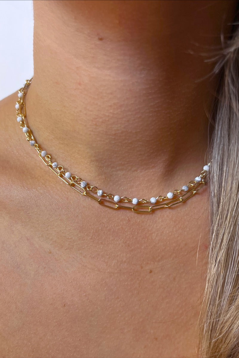 Front view of model wearing the Closer To You Necklace which features gold double chain link with white marble-like beads.