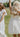 Image shows 2 young women outside in field. left woman is wearing a white maxi dress and left woman has her back turned and is wearing a white mini dress.