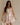 Image shows a brunette model. She is wearing a white, beige, and muted pink floral mini dress.