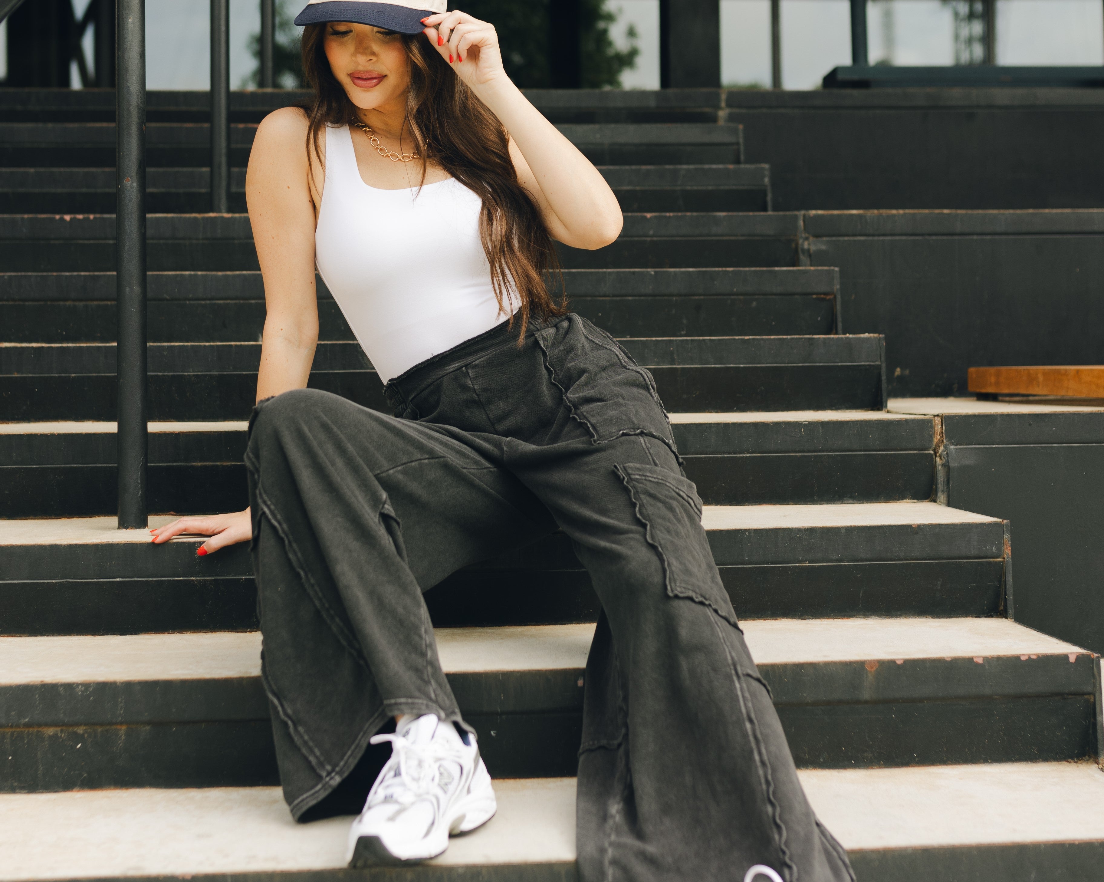 Lizard Thicket model is sitting on stairs, wearing black jeans and white tank top.