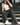 Lizard Thicket model is sitting on stairs, wearing black jeans and white tank top.