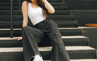 Lizard Thicket model is sitting on stairs, wearing black jeans and white tank top.