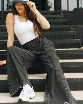 Lizard Thicket model is sitting on stairs, wearing black jeans and white tank top.