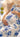 image shows blonde female model laying down on blanket while holding pregnant belly. Model is wearing white dress with blue floral print.