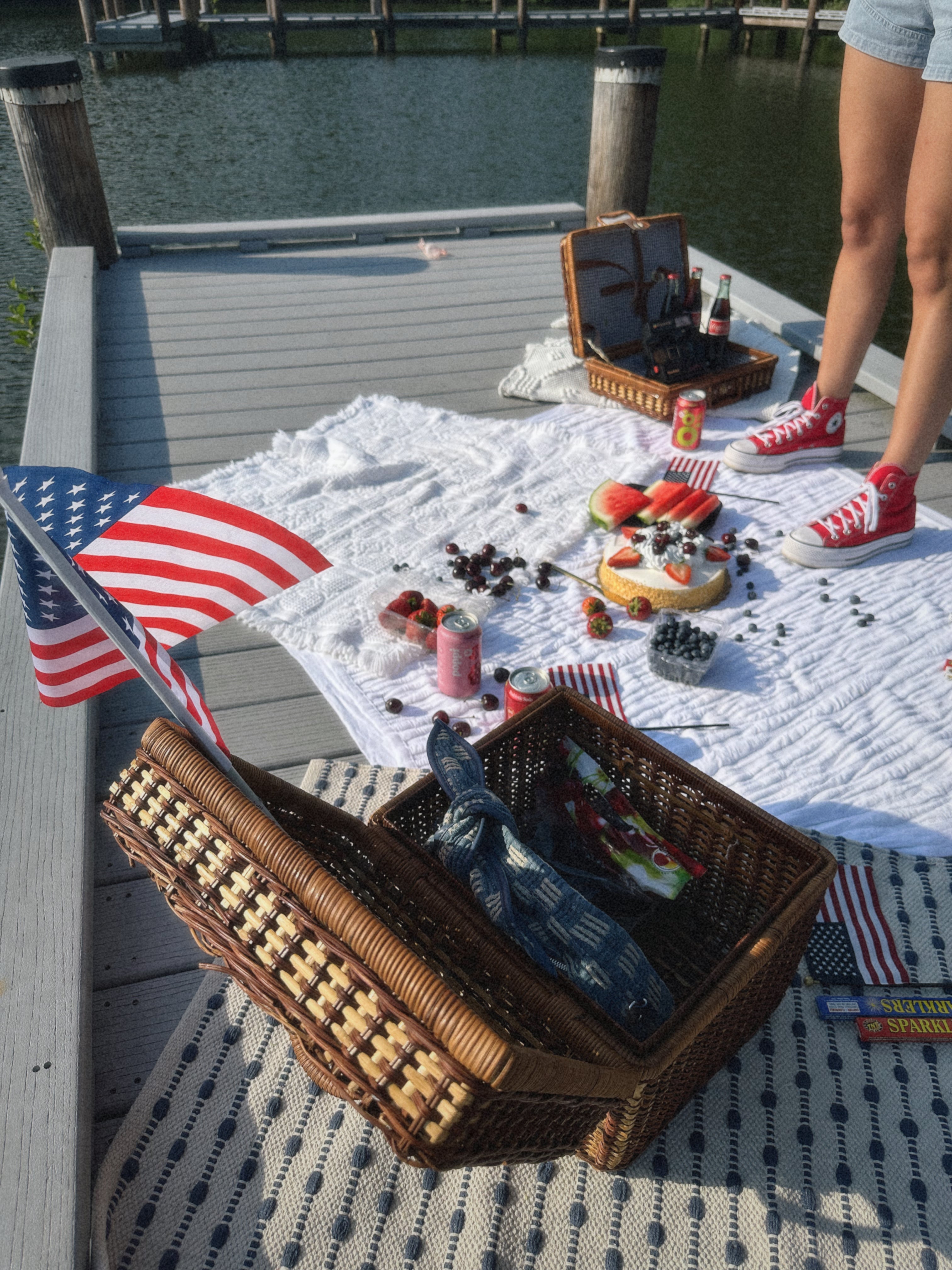 image of a 4th of july picnic with berries, cake & american flag in the background by a picnic basket