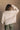 Back view of model wearing the Kaitlyn Beige Turtleneck Sweater that has beige knit fabric, ribbed hem, a ribbed turtleneck neckline, and long sleeves with ribbed cuffs.