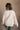 Back view of model wearing the Kaitlyn Beige Turtleneck Sweater that has beige knit fabric, ribbed hem, a ribbed turtleneck neckline, and long sleeves with ribbed cuffs.