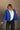 front view of model wearing the Ember Blue Corduroy Puffer Jacket that has royal blue corduroy fabric with a quilted design, pockets, a hidden zipper, a high neck, a drawstring, and long sleeves.