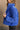 side view of model wearing the Ember Blue Corduroy Puffer Jacket that has royal blue corduroy fabric with a quilted design, pockets, a hidden zipper, a high neck, a drawstring, and long sleeves.