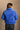 back view of model wearing the Ember Blue Corduroy Puffer Jacket that has royal blue corduroy fabric with a quilted design, pockets, a hidden zipper, a high neck, a drawstring, and long sleeves.