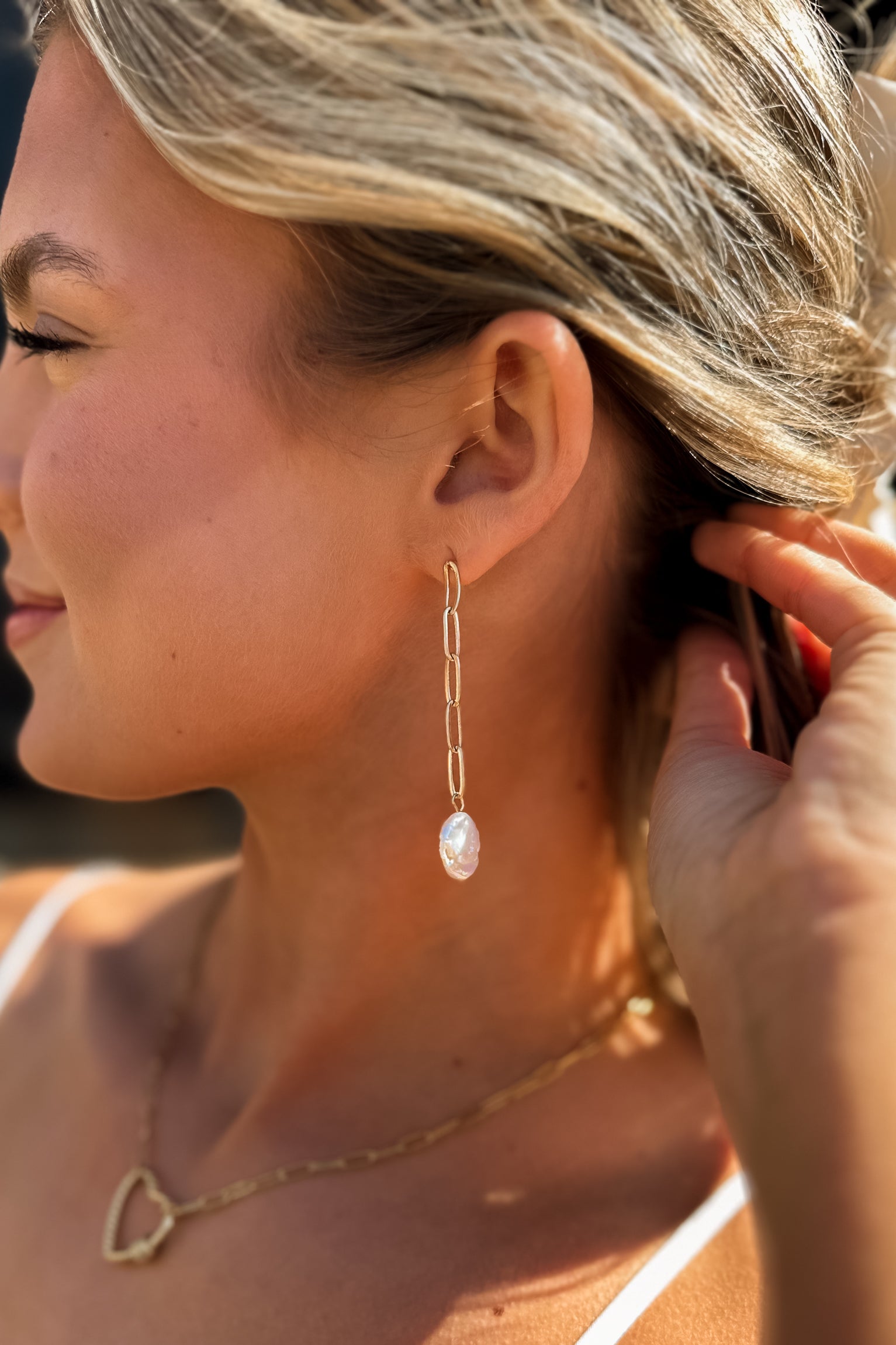 Side view of female model wearing the Layla Gold Chain & Flat Pearl Dangle Earring which features gold chain dangle earrings with flat pearl medallion