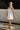 Full body side view of female model wearing the Camila Sleeveless Bubble Mini Dress in White which features Lightweight Fabric, Mini Length with Bubble Hem, Two Side Slit Pockets, Sweetheart Neckline, Adjustable Straps and Smocked Back