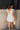 Back view of model wearing the Elena Blue Multi Floral Mini Dress which features ivory white, light green and blue sheer fabric, floral print, ivory lining, mini length, plunge neckline, ruffle straps, sleeveless and open back with bow tie closure.