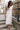 Full body view of model wearing the Eliana White Floral Midi Dress which features white sheer net fabric, white floral 3D pattern, midi length, white lining, overlap plunge neckline, thick straps with tie details, sleeveless and monochrome back zipper wit