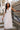 Full body view of model wearing the Eliana White Floral Midi Dress which features white sheer net fabric, white floral 3D pattern, midi length, white lining, overlap plunge neckline, thick straps with tie details, sleeveless and monochrome back zipper wit