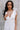 Close up view of model wearing the Eliana White Floral Midi Dress which features white sheer net fabric, white floral 3D pattern, midi length, white lining, overlap plunge neckline, thick straps with tie details, sleeveless and monochrome back zipper with