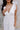 Close up view of model wearing the Eliana White Floral Midi Dress which features white sheer net fabric, white floral 3D pattern, midi length, white lining, overlap plunge neckline, thick straps with tie details, sleeveless and monochrome back zipper with