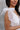 Side view of model wearing the Eliana White Floral Midi Dress which features white sheer net fabric, white floral 3D pattern, midi length, white lining, overlap plunge neckline, thick straps with tie details, sleeveless and monochrome back zipper with hoo