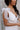 Side view of model wearing the Eliana White Floral Midi Dress which features white sheer net fabric, white floral 3D pattern, midi length, white lining, overlap plunge neckline, thick straps with tie details, sleeveless and monochrome back zipper with hoo