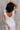 Close up back view of model wearing the Eliana White Floral Midi Dress which features white sheer net fabric, white floral 3D pattern, midi length, white lining, overlap plunge neckline, thick straps with tie details, sleeveless and monochrome back zipper