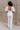 Full body back view of model wearing the Bella Ivory Plunge Neckline Flare Jumpsuit which features white knit fabric, plunge neckline, short flare sleeves, open back, monochrome back zipper with hook closure and flare pant legs.