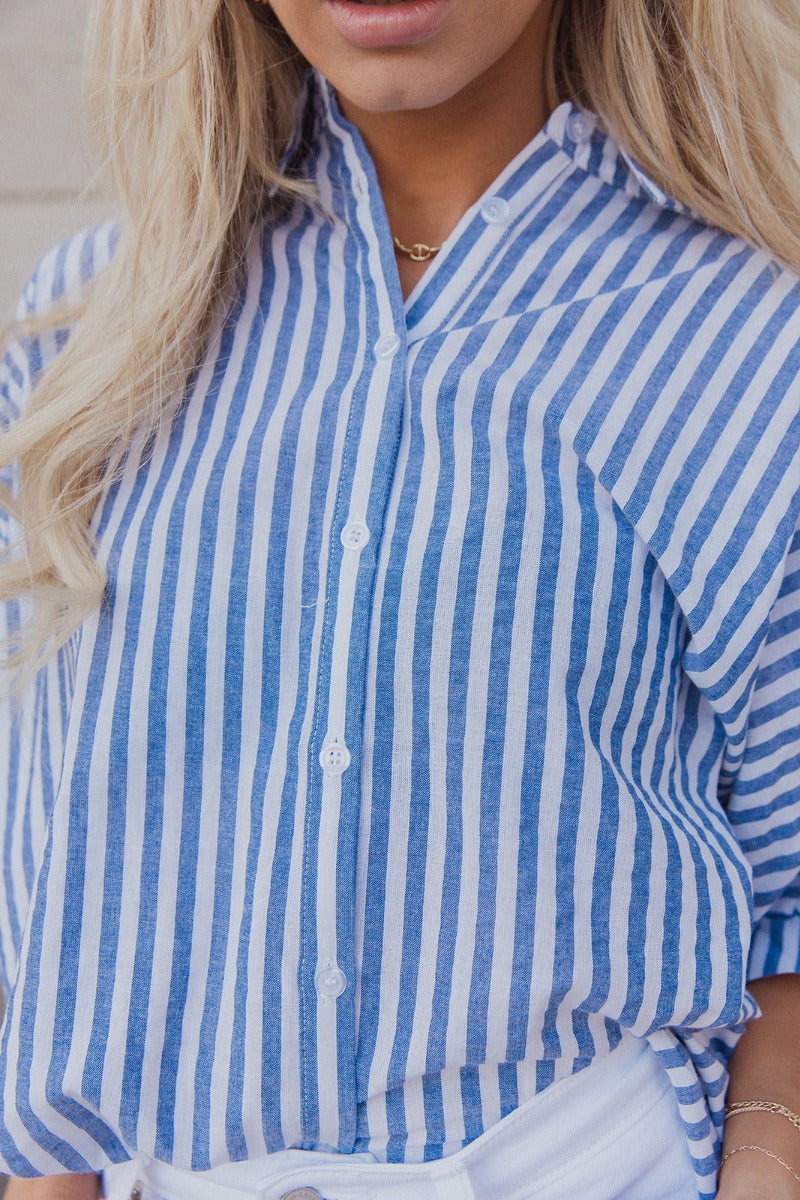 Close up view of model wearing the Ella Blue & White Stripe Button Up Top which features dark blue and white fabric with a striped pattern, white button-up front closures, an oversized fit, a collared neckline and short sleeves with cuffs.