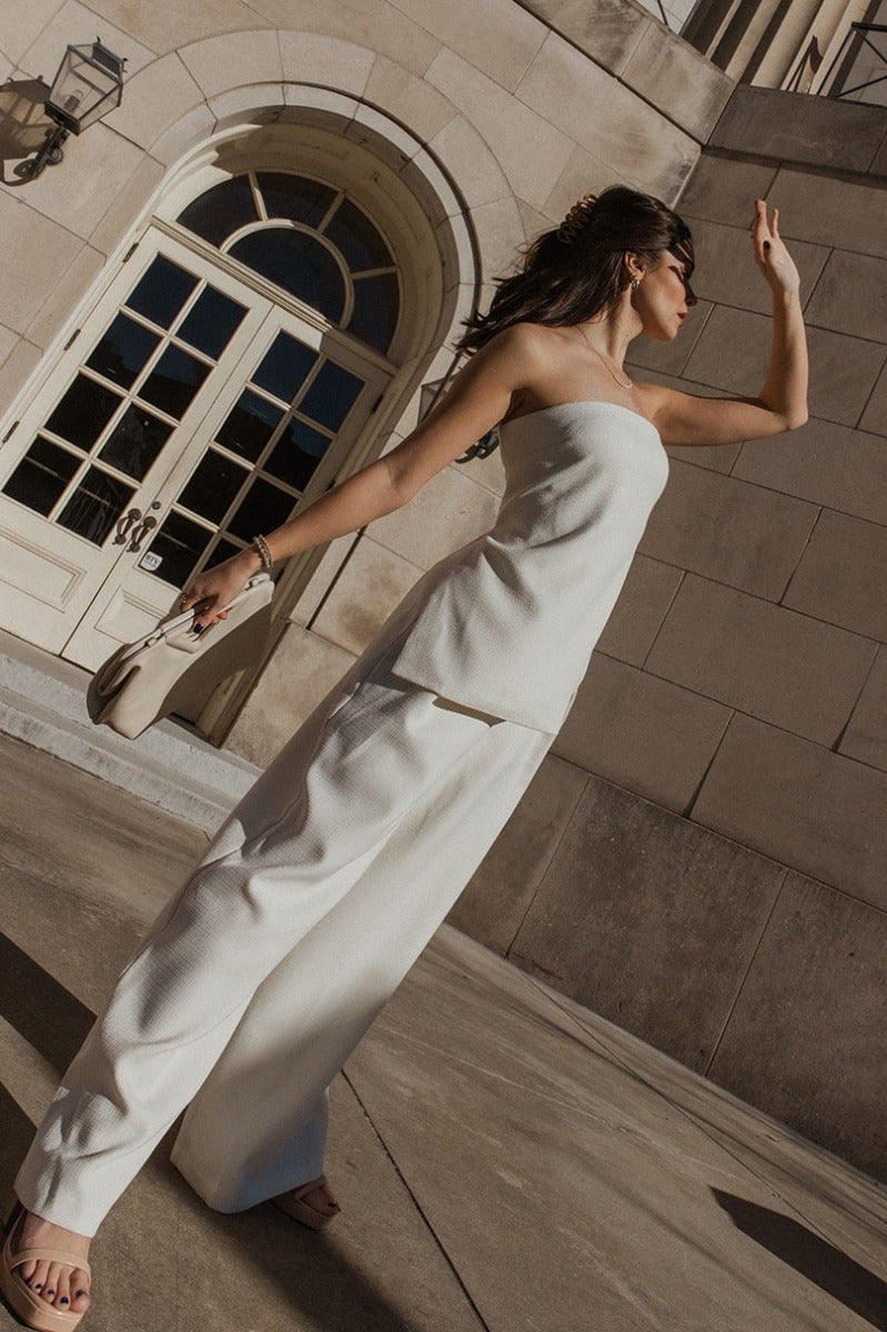 Full body view of model wearing the Grace Ivory Wide Leg Pants which features ivory textured fabric, two side slit pockets, monochrome side pockets, and wide pant legs.