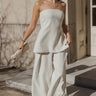 Full body view of model wearing the Grace Ivory Side Slits Strapless Top which features ivory textured fabric, side high slit details, a strapless neckline, and a monochrome back zipper with a hook closure.