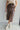 front view of model wearing the Trouble Maker Pleather Midi Skirt that has dark brown faux leather, midi length, a slit, pockets, a front zipper, and belt loops