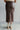 back view of model wearing the Trouble Maker Pleather Midi Skirt that has dark brown faux leather, midi length, a slit, pockets, a front zipper, and belt loops