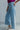 Side view of model wearing the Ceros: Here Not There Jeans which features light denim wash fabric, two front pockets, two back pockets, front zipper with button closure, belt loops, super high waisted, wide cropped flares and distressed hem.