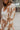 Close-up side view of model wearing the In Your Dreams Top, that has an ivory knit material, a mocha geometric print, a collar neck, a long sleeve, and a button-up front. Worn over whit tank with with matching skirt.