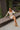 Full body view of model wearing the Take Your Time Dress, which features an ivory knit material, a taupe striped pattern, a straight neckline, a long sleeve, a mini length, and a tight fit. Model is sitting.