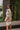 Back/side view of model wearing the Take Your Time Dress, which features an ivory knit material, a taupe striped pattern, a straight neckline, a long sleeve, a mini length, and a tight fit.