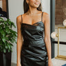Front view of model wearing the Big Reputation Dress, which features a black faux-leather material, a surplice, sweetheart neckline, a sleeveless design with thin adjustable straps, a draped front, a surplice bottom, and a zip-up back closure