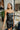 Front view of model wearing the Big Reputation Dress, which features a black faux-leather material, a surplice, sweetheart neckline, a sleeveless design with thin adjustable straps, a draped front, a surplice bottom, and a zip-up back closure