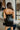 Back view of model wearing the Big Reputation Dress, which features a black faux-leather material, a surplice, sweetheart neckline, a sleeveless design with thin adjustable straps, a draped front, a surplice bottom, and a zip-up back closure