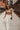 Full body front view of model wearing the Get In Line Top, that has a brown knit material, a patchwork design, a high neckline, a long sleeve, and lettuce edge hems