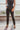 Frontal view of the Next Level Straight Leg Pants that features a black faux-leather material, a high-rise fit, a clasp and zipper front closure, belt loops, two front pockets, a middle seam down the legs, and a straight leg fit.