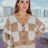 Front view of model wearing The Check Please Cardigan features a khaki colored knit material, a white checkered pattern, a four button-up front, and long sleeves.