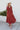 Full body front view of model wearing the Seasons Change Maxi Dress, which has a rust colored fabric, a V neckline, long sleeves, a button-up front, a babydoll design, a midi length, and a flowy fit.