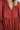 Close-up view of neckline- model is wearing the Seasons Change Maxi Dress, which has a rust colored fabric, a V neckline, long sleeves, a button-up front, a babydoll design, a midi length, and a flowy fit.